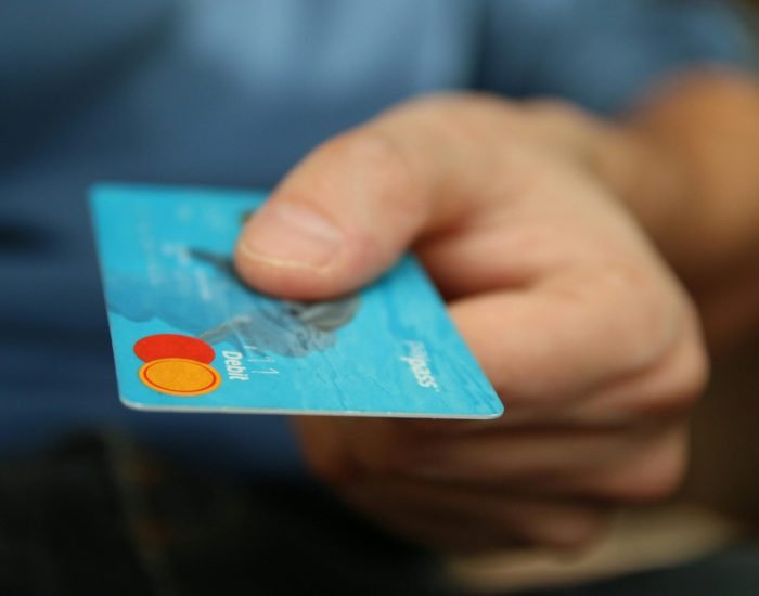 A close-up shot of a hand offering a blue debit card for payment.